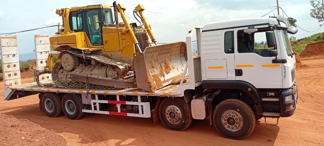 White rigid lowbed truck carrying a Caterpillar dozer on a red-earth road