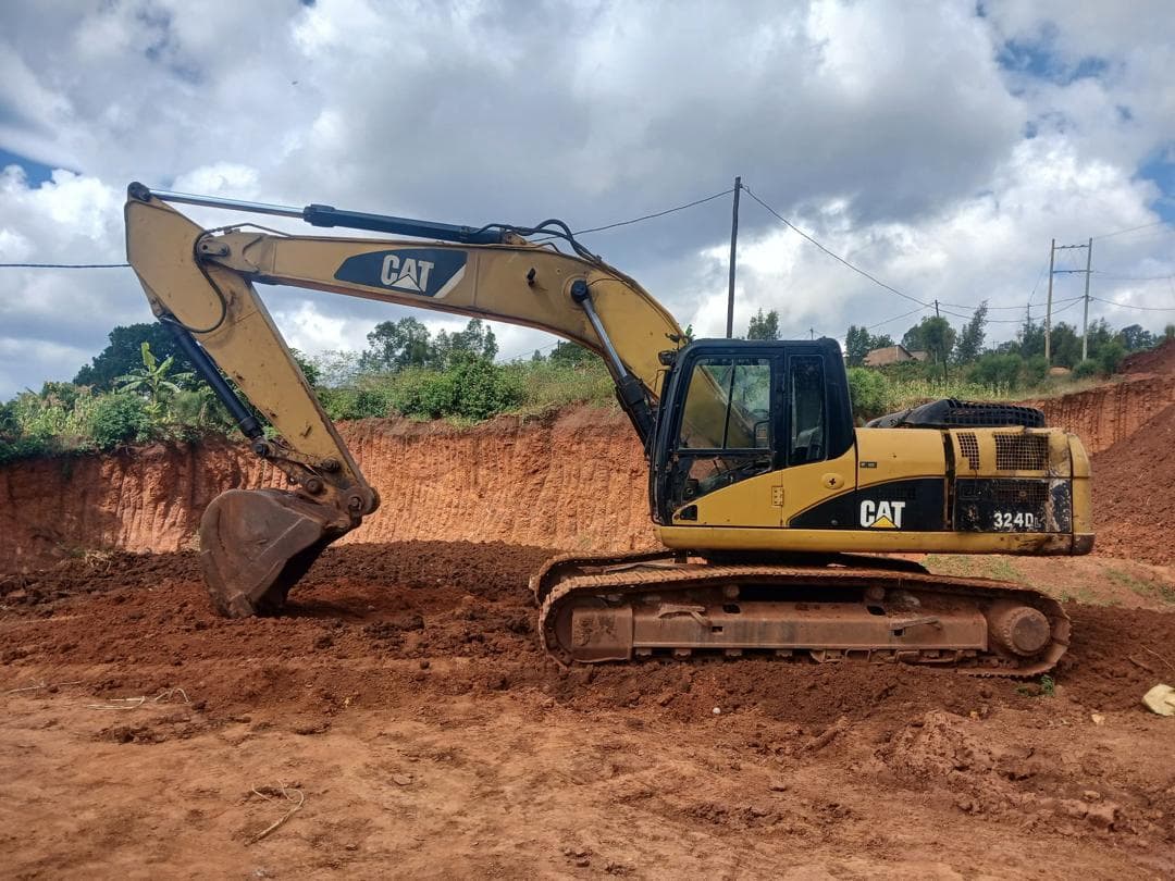 Caterpillar 324D excavator cutting into a red-earth bank outside Kigali